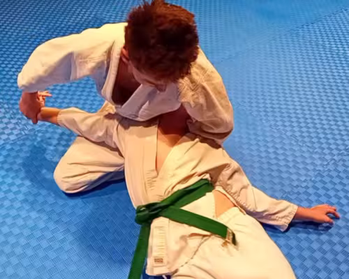 Zwei Aikidoka &uuml;ben auf einer blauen Matte eine Bodentechnik mit einem Armhebel.